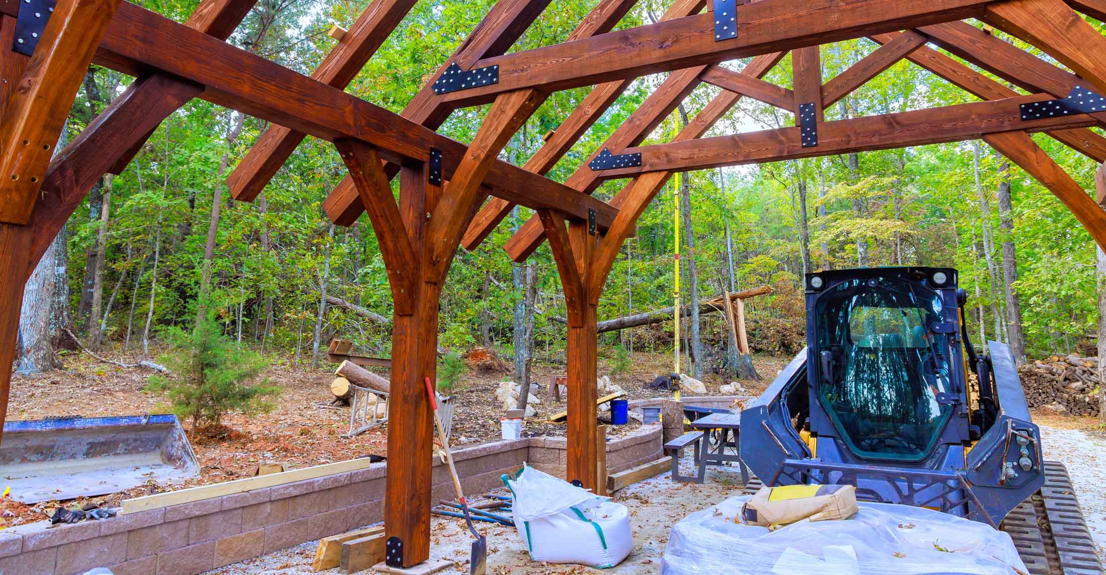 Skid steer finishing the grounds around a new timber-frame pavilion