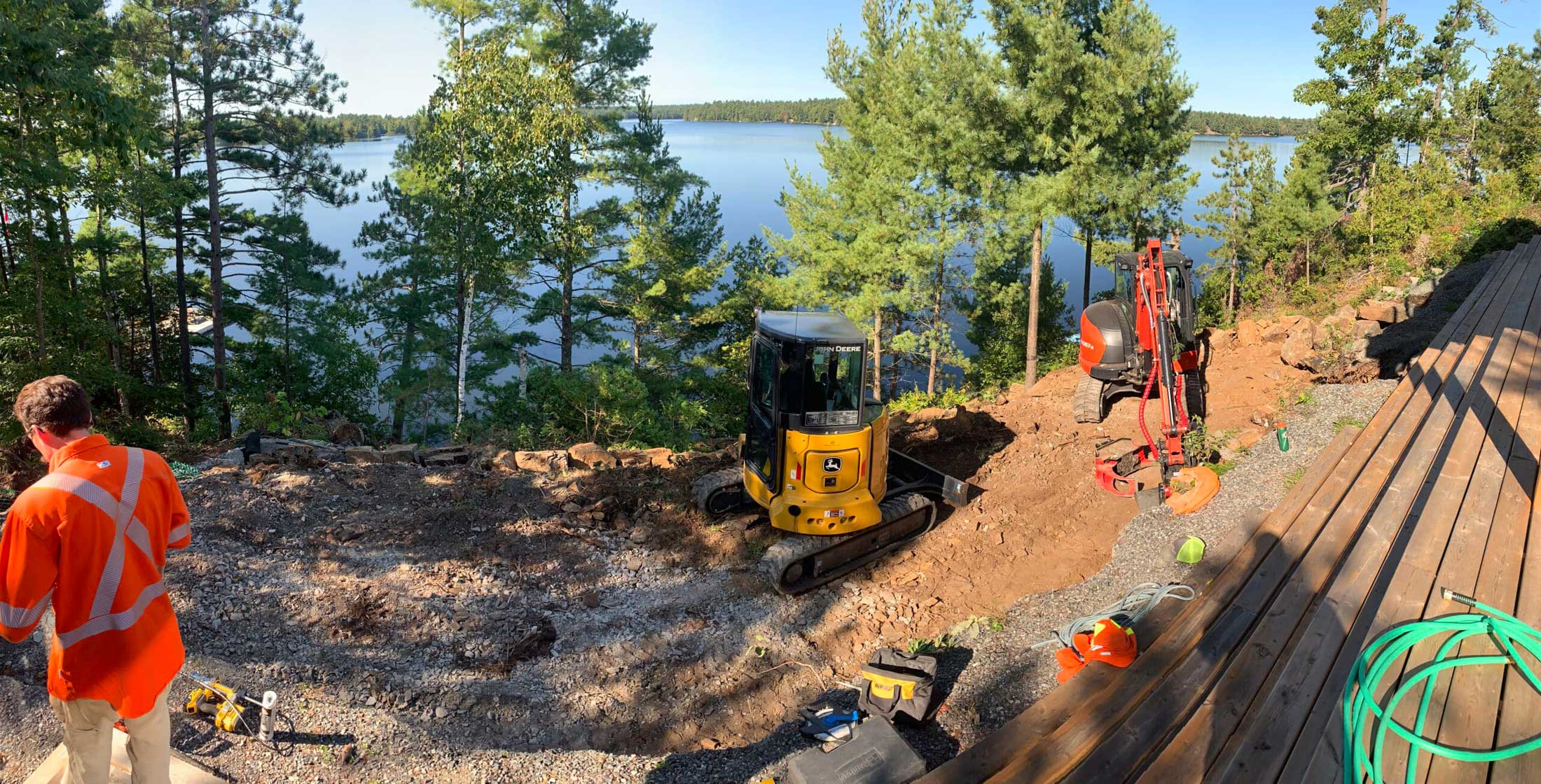 Two mini excavators working on a lakeside cottage lot